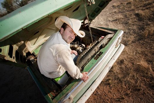Man in cowboy hat under the hood of truck