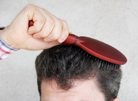 Mature man brushing black greyish hair with red hairbrush