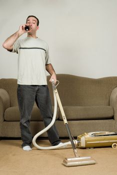 Full body view of a man drinking a beer at home while vacuuming the carpet