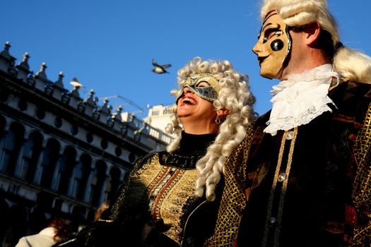 A couple with masks on the Piazza San Marco, Venice during the carnival, the woman laughing