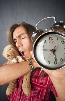 Sleepy handsome young man with long hair and alarm clock
