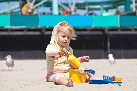 Cute little European toddler girl having fun with sand on the beach.