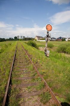 Railroad sing near track in the middle of meadow.