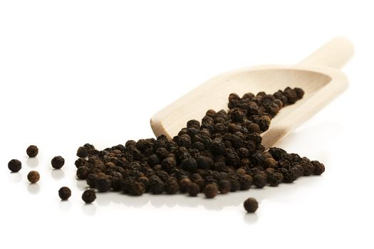 black peppercorns with a wooden shovel on white background