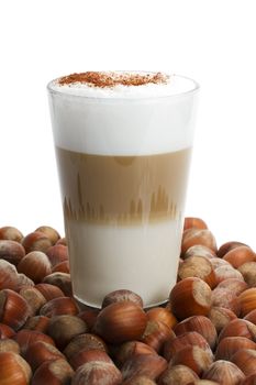 latte macchiato between a lot of hazelnuts on white background