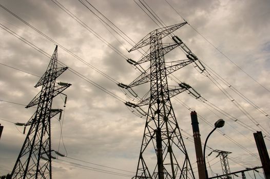 Silhouettes of electric pillars in dark cloudy sky