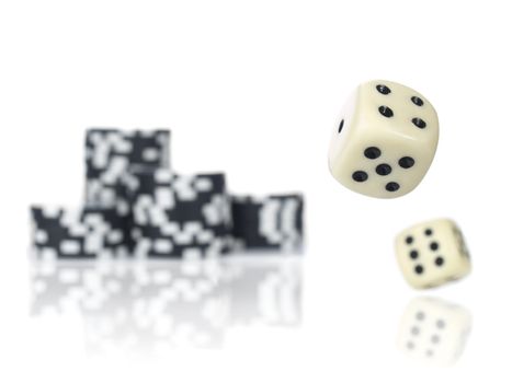 Pair of dice rolling in front of stacked black poker chips.