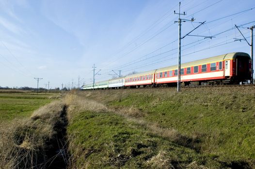 Train leaving Wroclaw city in Poland. Open field, green meadows at the beginning of spring.