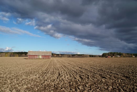 Dark cloud casting shadow over barn and ploughed field in autumn. Photographed in Salo, Finland October 2010.