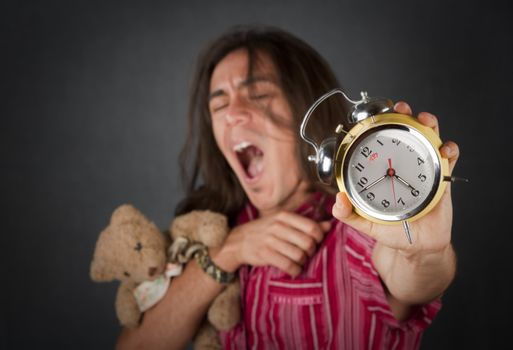 Sleepy handsome young man with long hair and alarm clock