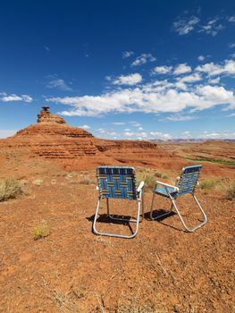 Two outdoor lawn chairs in scenic desert landscape with mesa land formation.