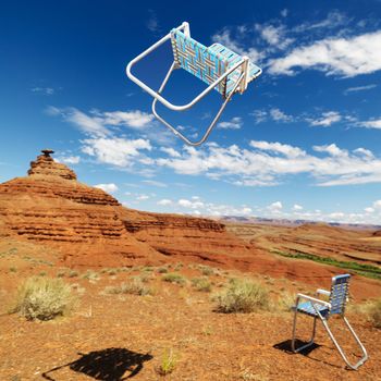 Lawn chair thrown in midair in scenic desert landscape with land formation.