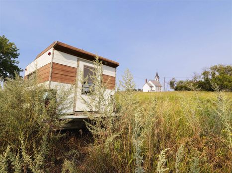 Recreational vehicle in overgrown field with rural church in distance.