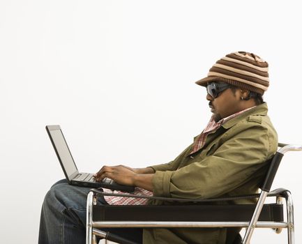Side view of African-American mid-adult man wearing hat and typing on laptop computer.