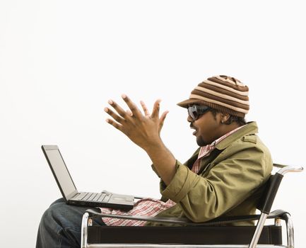 Side view of African-American mid-adult man wearing hat and making surprised expression at laptop computer.