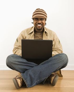 African-American mid-adult man sitting on floor smiling at viewer on laptop computer.