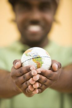 African-American mid-adult man wearing hat holding small globe toviewer.