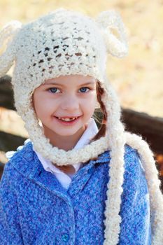 Beautiful little girl in a white bobble hat smiling at the camera. Shallow DOF.