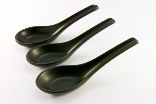 Three black chinese china soup spoons on a white background