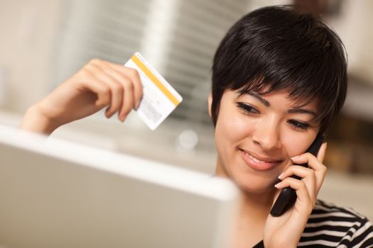 Pretty Young Multiethnic Woman Holding Phone and Credit Card Using Laptop.