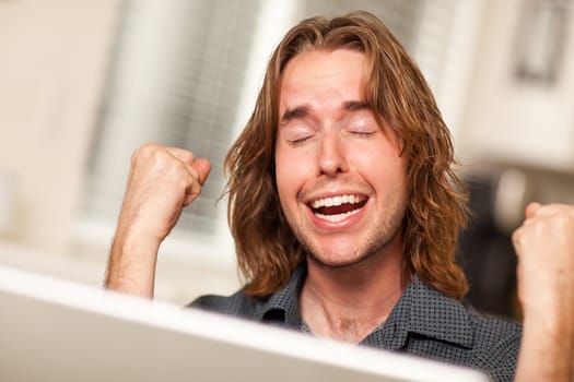 Young Man Using A Laptop Computer and Cheering with Fists in the Air.