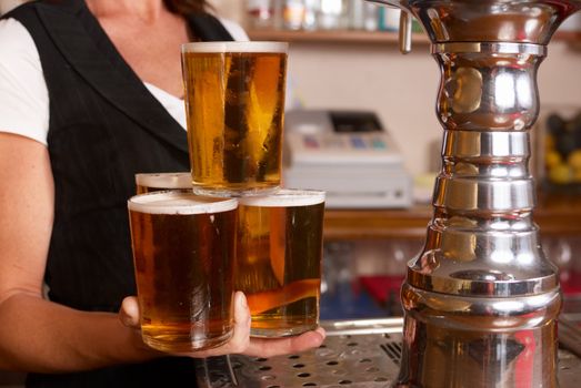 Skilful waitress holding four freshly filled pint glasses in one hand