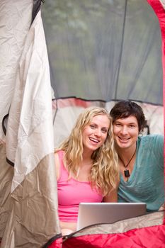 A portrait of a happy camping couple with a laptop, smiling at the camera