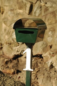 green mailbox with white number one on it, behind it is a stone wall