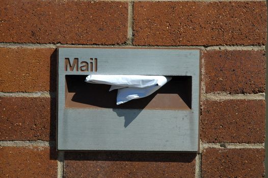 grey mailbox in a red brick wall, white paper in it