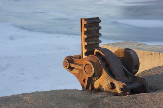 rusty lifting gear of irrigation ditch headgate against a frozen river