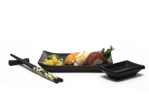 A set of sushi on a black plate with wasabi and gari, isolated on a white background, wish hashi ans soy sauce.