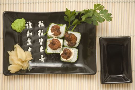 A set of sushi on a black plate with wasabi and gari, on a makisu (bamboo rolling mat).