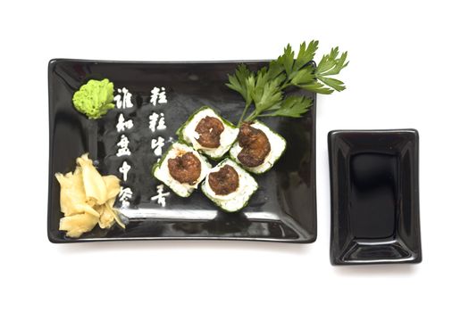 A set of sushi on a black plate with wasabi and gari, isolated on a white background.