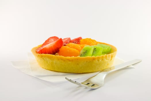 Strawberry, mandarin and kiwi custard fruit tart on a napkin with fork on a  white background