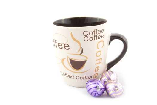 cup with text coffee with some chocolate eastern eggs next to it isolated on white