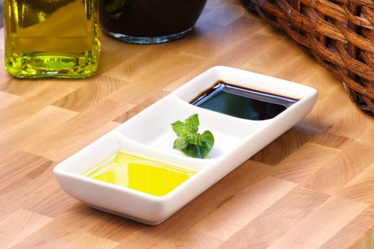 fresh first cold pressed extra virgin olive oil and balsamic vinegar on top af a fine wood cutting board garnished with basil blossom