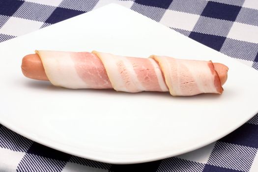 raw hot dog rapped in bacon o white plate  
