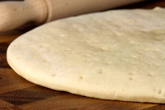pizza  dough sheeet  on  wood cutting board with rolling pin