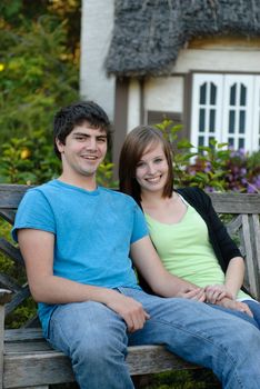 Two young teens smiling and sitting on a park bench outside