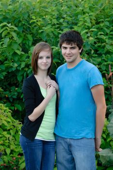 A young couple standing next to each other with green leaves in the background.