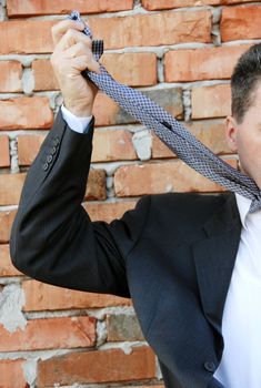 businessman smothering himself with necktie by brick wall