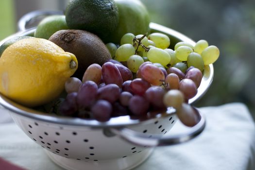 Fresh lemons, limes, grapes and kiwi in colander