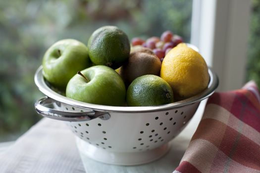 Fresh lemons, limes, grapes and kiwi in colander