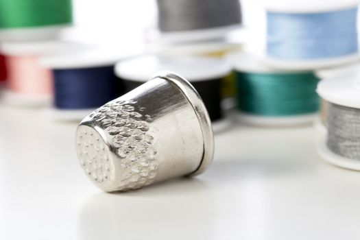 Metal thimble in front of spools of thread.