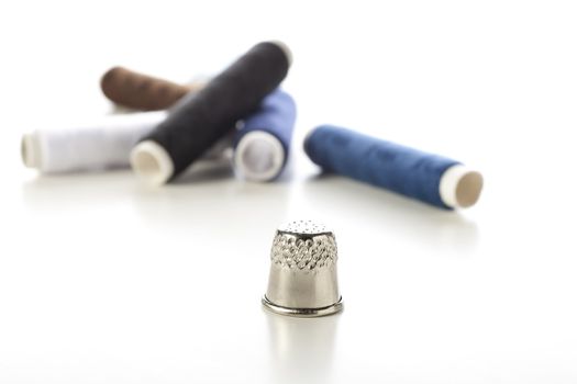 Thimble and blue and brown thread on white background.