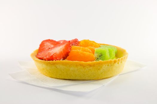 Strawberry, mandarin and kiwi custard fruit tart on a napkin with a white background