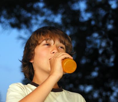 Teenage boy drinking orange drink from a glass bottle with dark skies in the background.