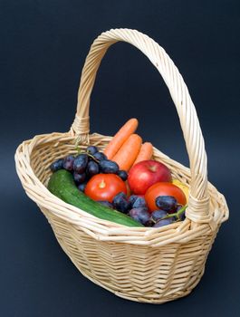 Vegetables and fruits in a basket. Against a dark background.