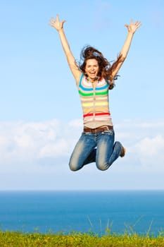 A beautiful young woman jumping up in the air smiling outdoors by a beautful ocean