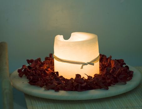 Great white candle surrounded with red rose petals